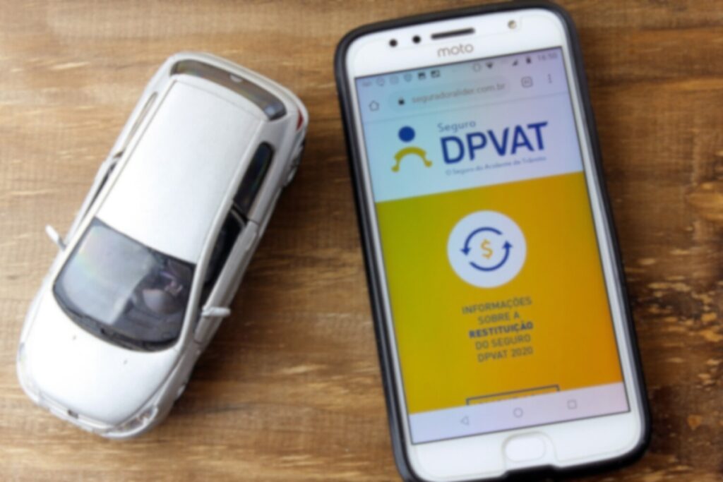 Celular com site do Seguro DPVAT, carro miniatura.
